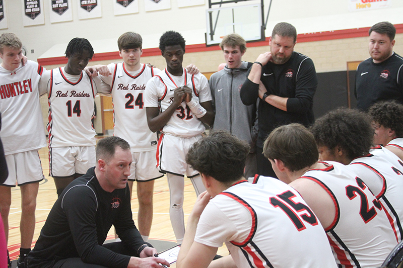 The Huntley boys basketball team listens as coach Colin Kalamatas gives instructions during a timeout against Burlington Central. The Red Raiders outlasted the Rockets, 73-68, in three overtimes Feb. 2.